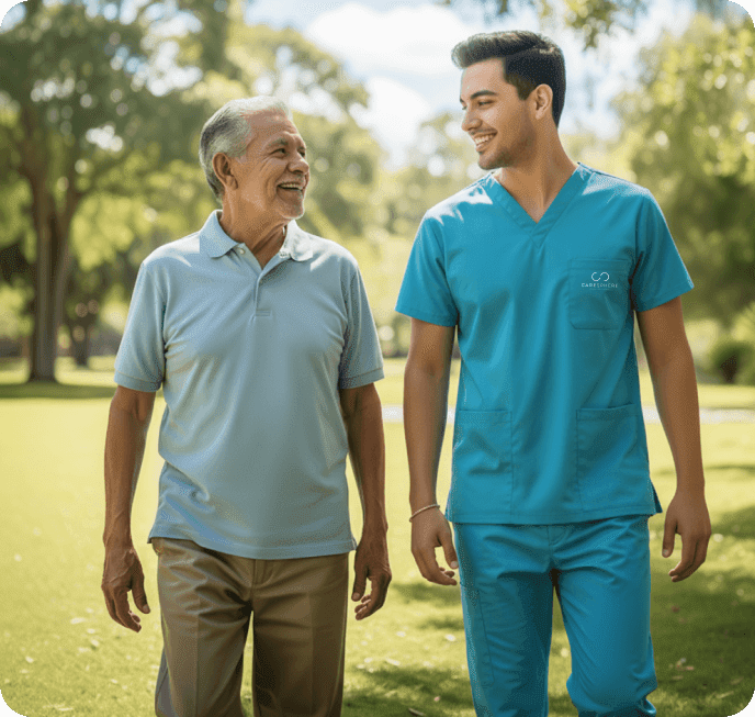 Older man and younger man in teal medical scrubs walking together in sunny park