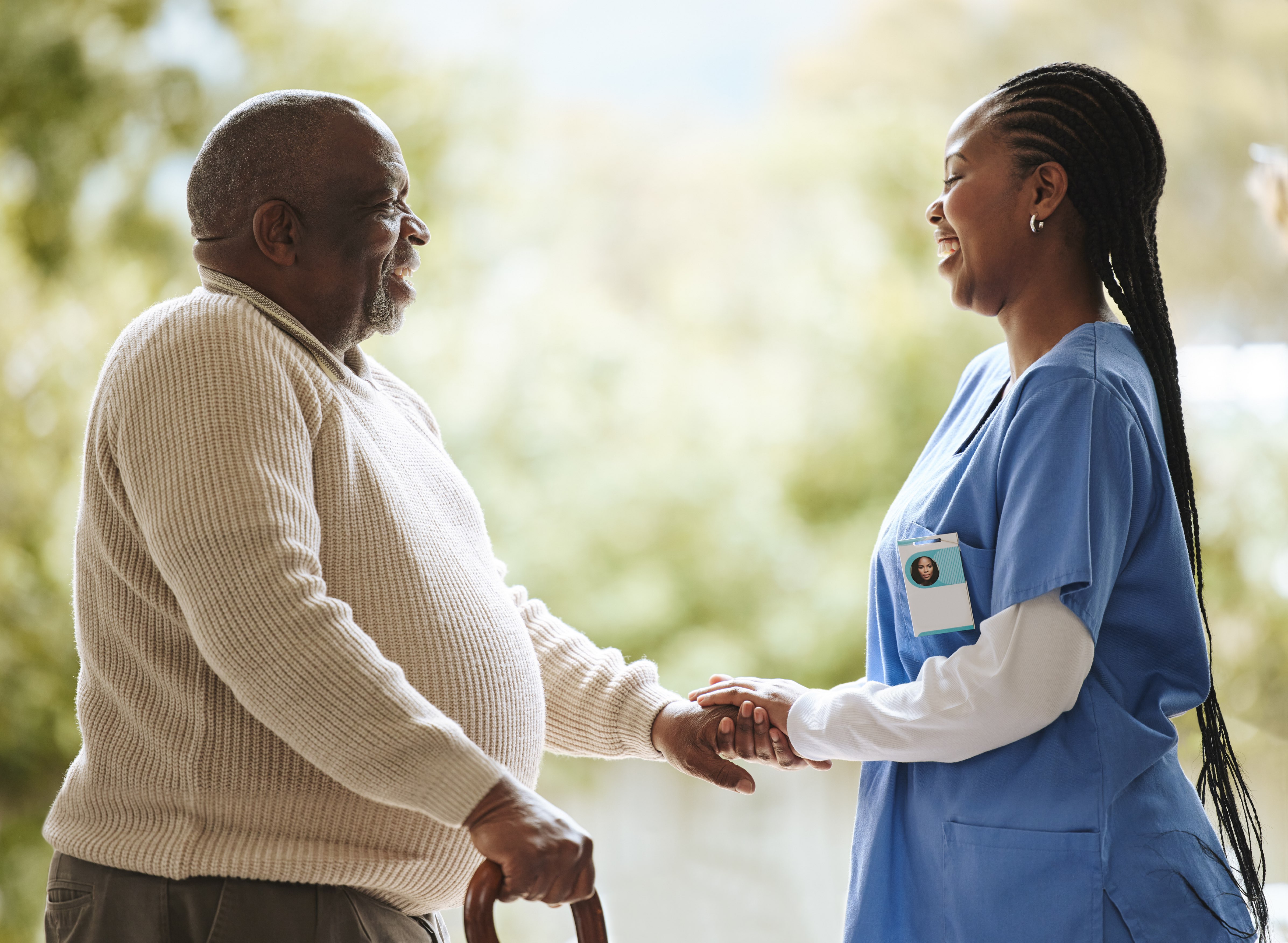 Senior man with a cane smiling while holding hands with a caregiver outdoors.